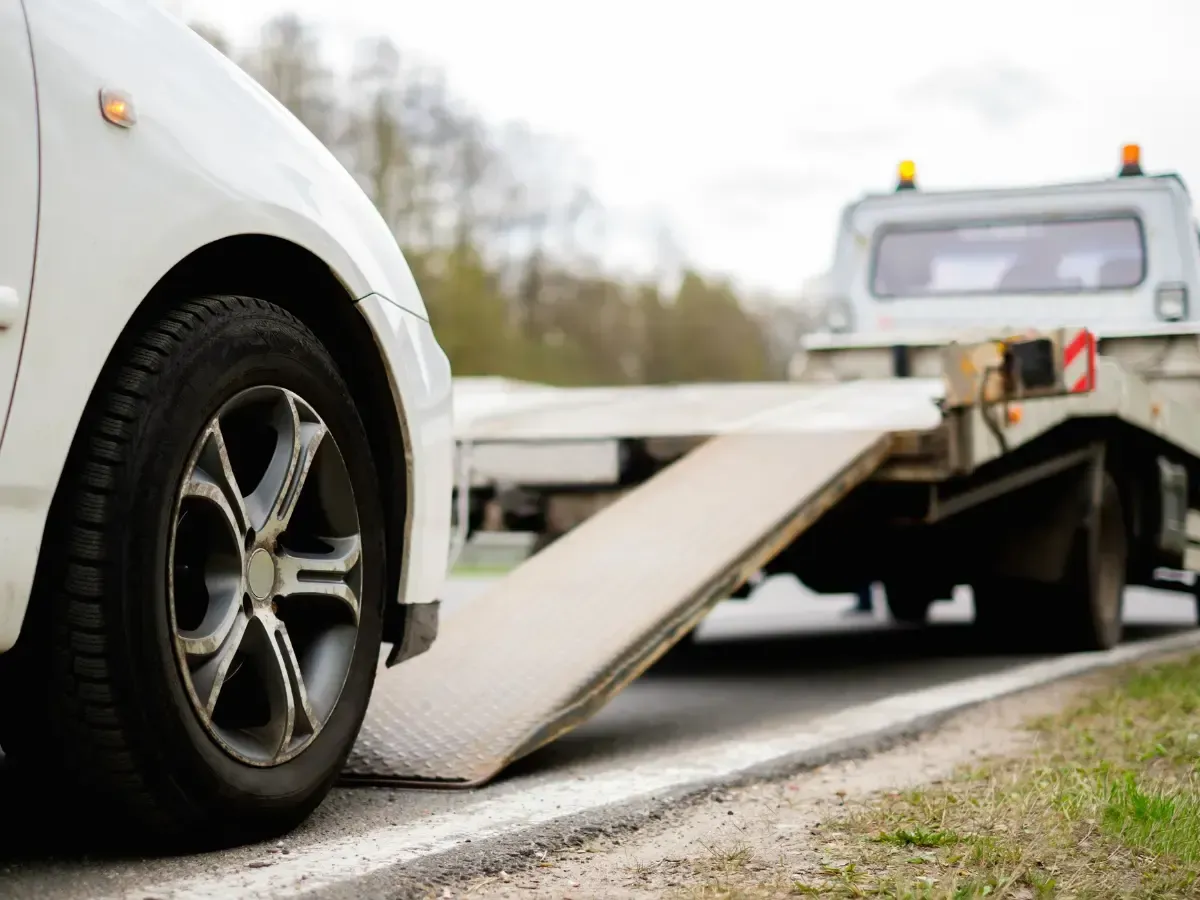 A white car is being towed by a tow truck.