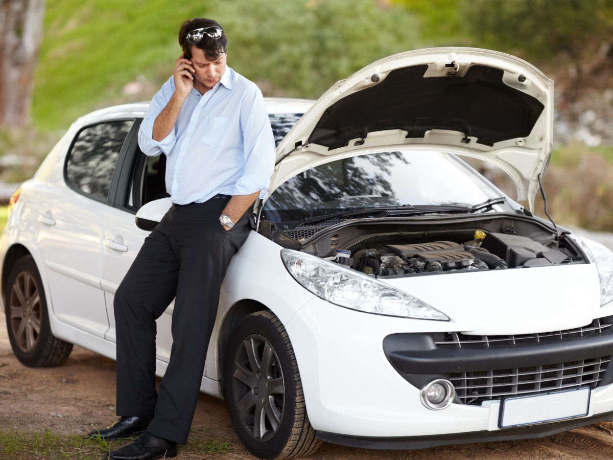 A man leaning against a broken down car talking on a cell phone