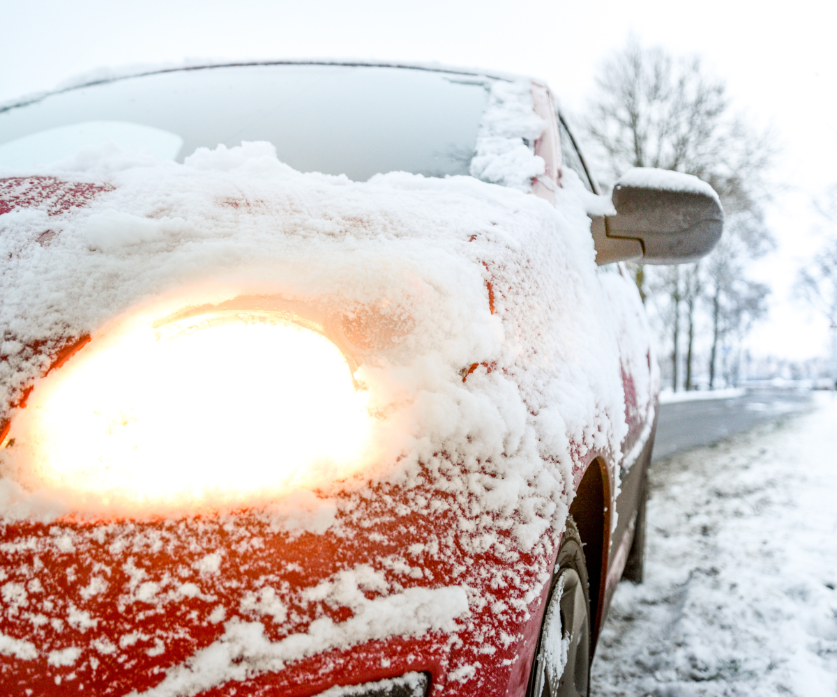A red car is covered in snow and has its headlights on. A red car is covered in snow and has its headlights on.