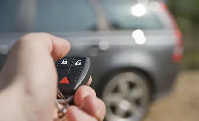 A person is holding a remote control in front of a car. A person is holding a remote control in front of a car.