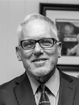 A man in a suit and tie is smiling in a black and white photo.
