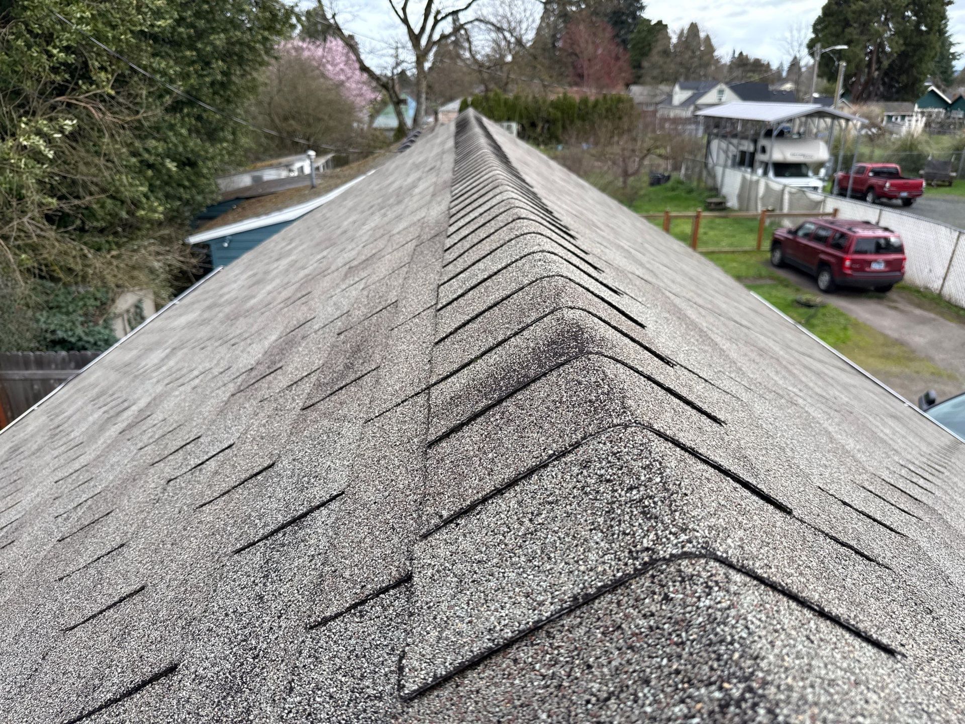 Gravel roof ridge on a suburban house, viewed from above with houses and trees in the background
