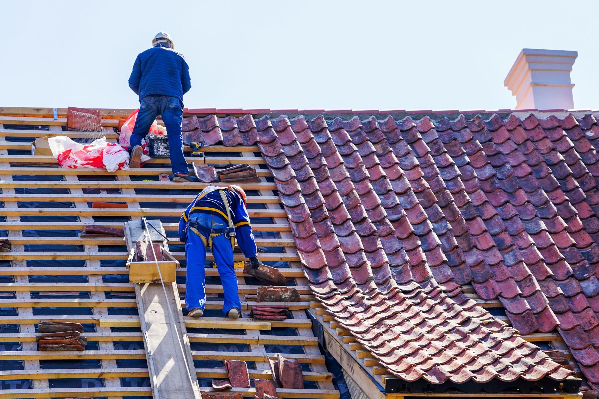 Workers repairing a red-tiled roof with scaffolding and wooden planks.