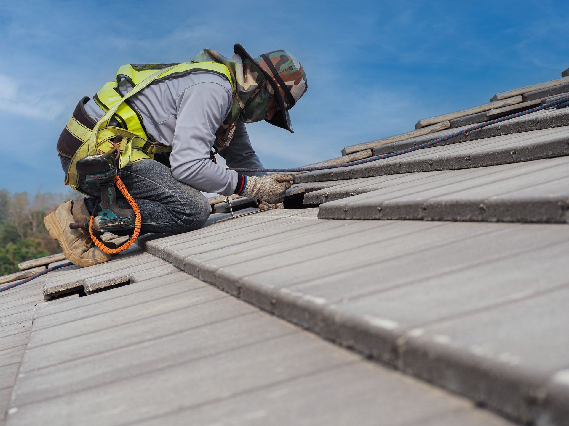 Roofer in a harness nails new shingles into place on a steep roof during roof replacement services. Roofer in a harness nails new shingles into place on a steep roof during roof replacement services.