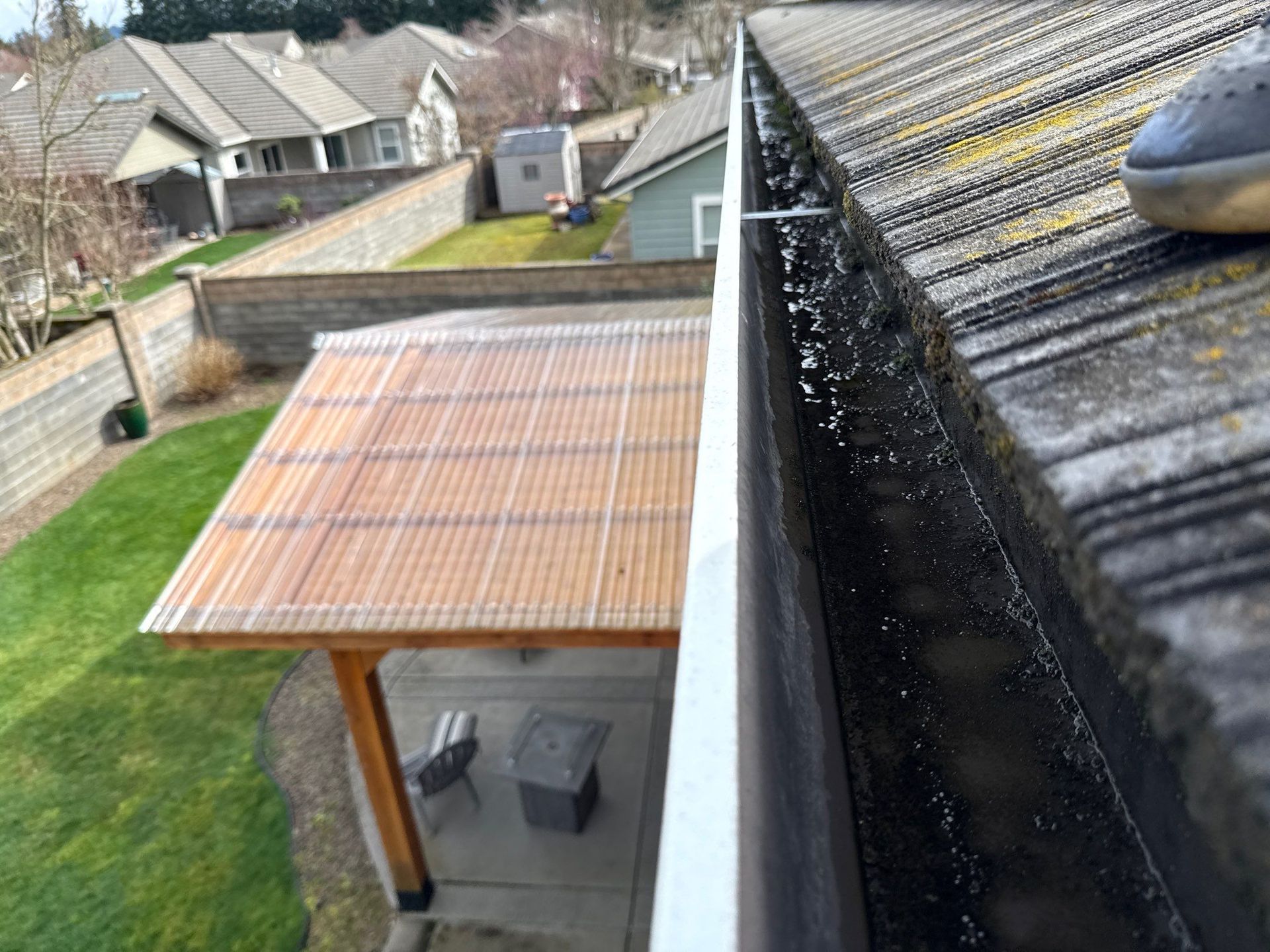 Rainwater dripping from a roof gutter beside a wooden patio cover in a suburban backyard.