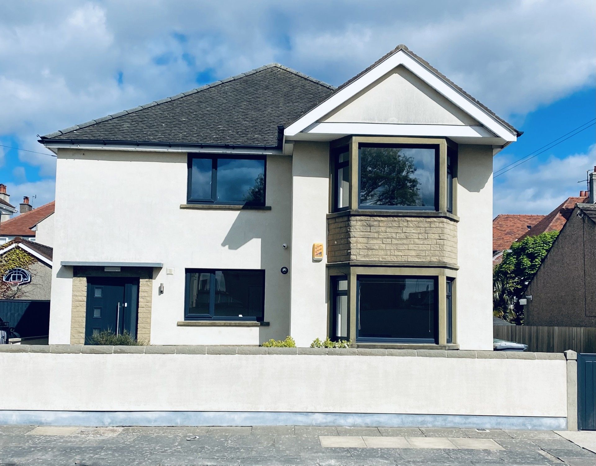 Buttermere House. Modern two-story white house with dark roof, front wall, and large windows under a blue sky