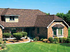 A large brick house with a brown roof and a large lawn in front of it.