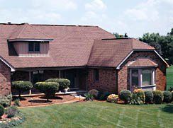 A large brick house with a brown roof and a large lawn in front of it.
