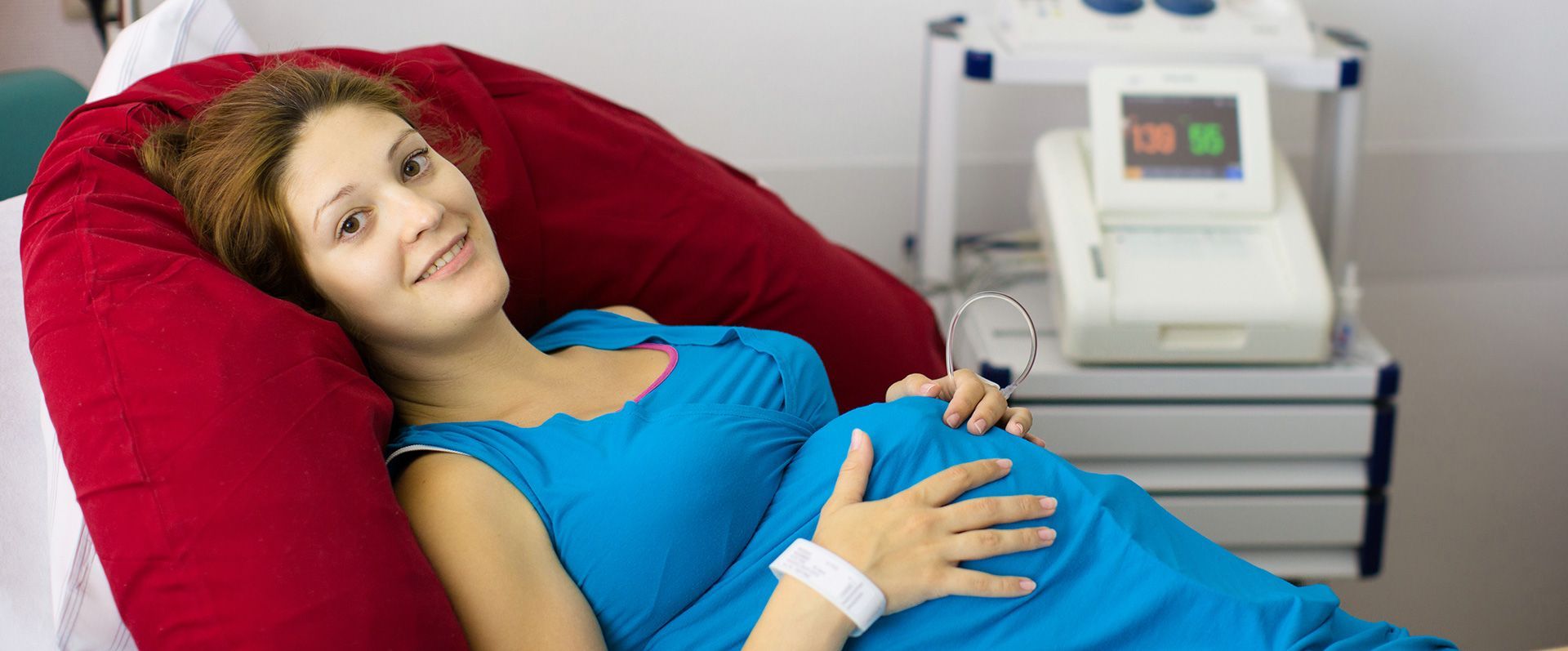 Woman lying on a hospital bed, smiling, with a medical monitor beside her.