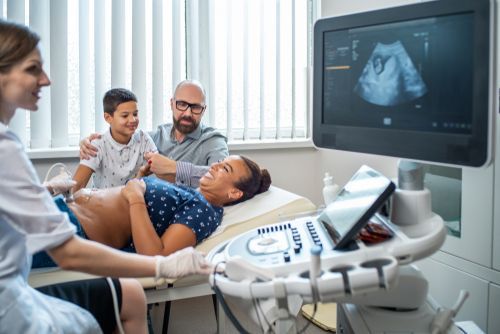 Doctor and family in an ultrasound exam room, viewing a pregnancy scan on a monitor.