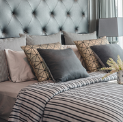Bed with gray tufted headboard, striped comforter, and various decorative pillows.