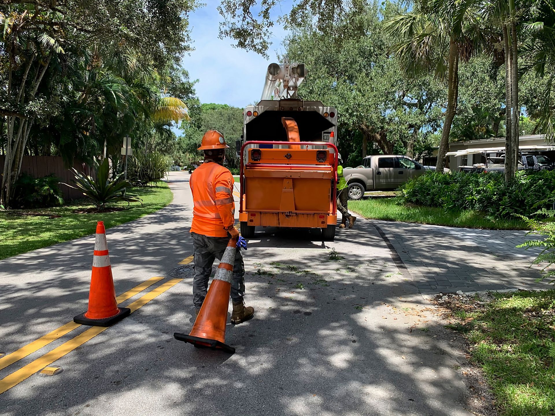 Orange road worker beside traffic cones and a truck on a tree-lined street Orange road worker beside traffic cones and a truck on a tree-lined street