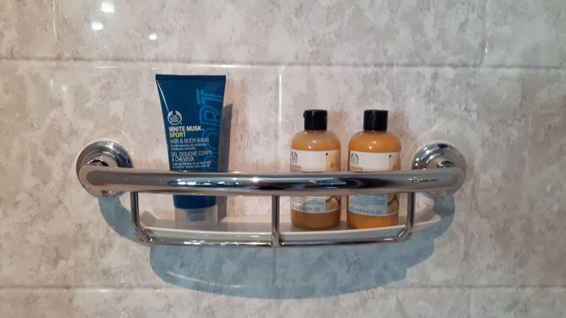 A bathroom shelf with two bottles of shampoo and a tube of lotion.