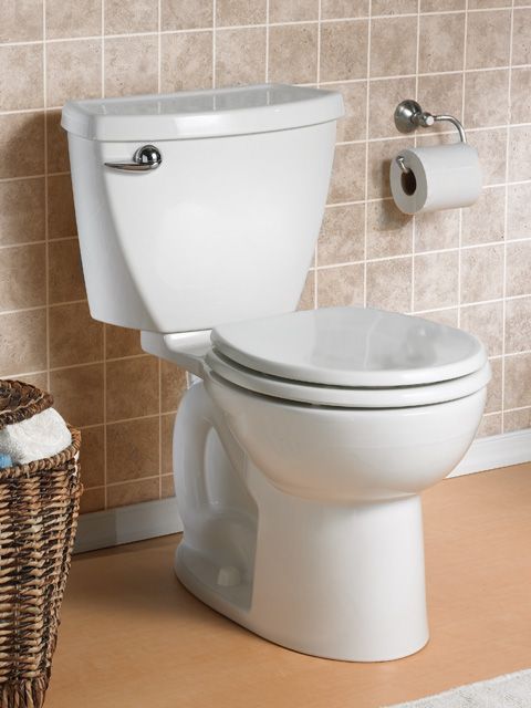 A white toilet in a bathroom next to a basket of towels