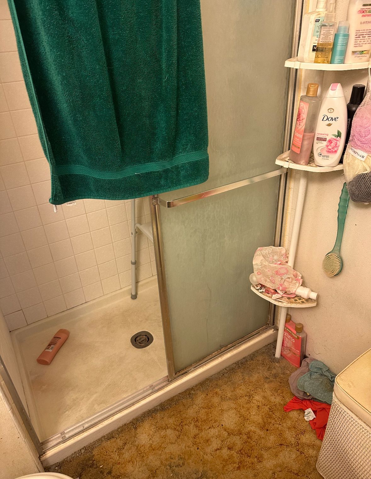 A bathroom with a green towel hanging over the shower door.