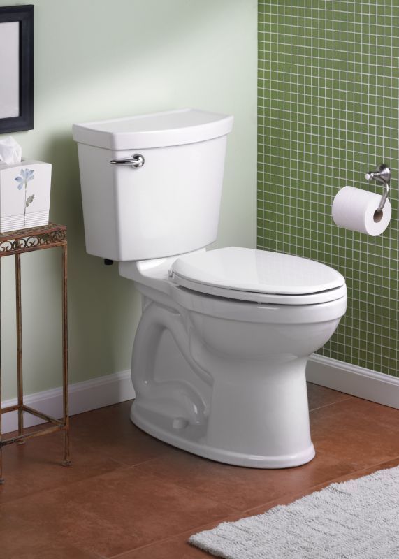 A white toilet is in a bathroom next to a green tiled wall.