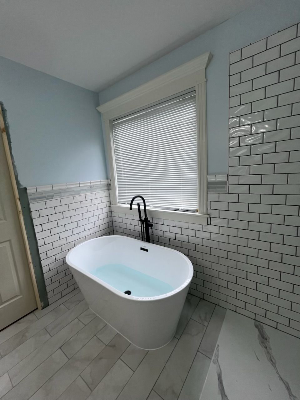 A bathtub in a bathroom next to a window with blinds.