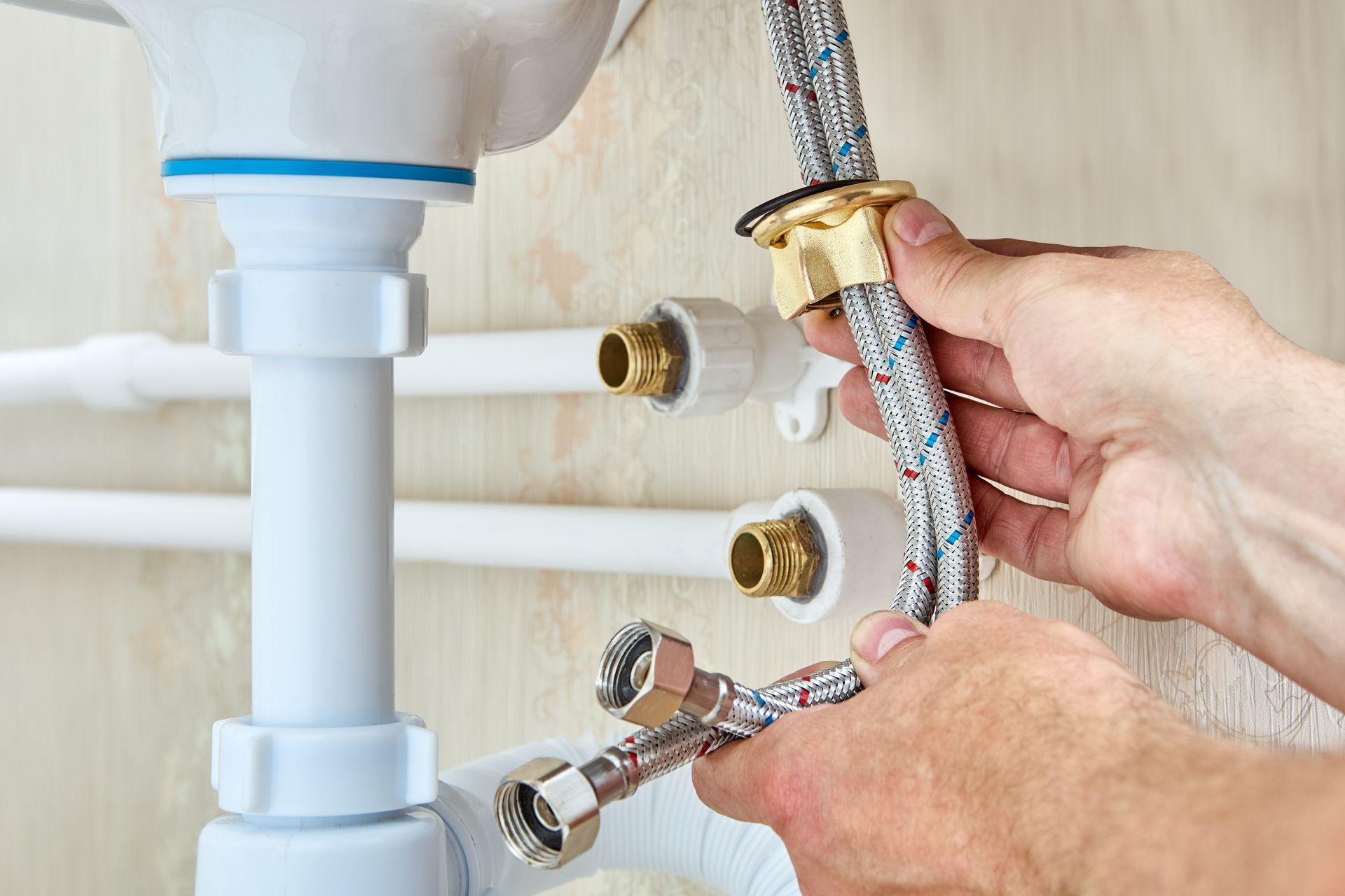 Plumber connecting braided water supply lines under a white sink.