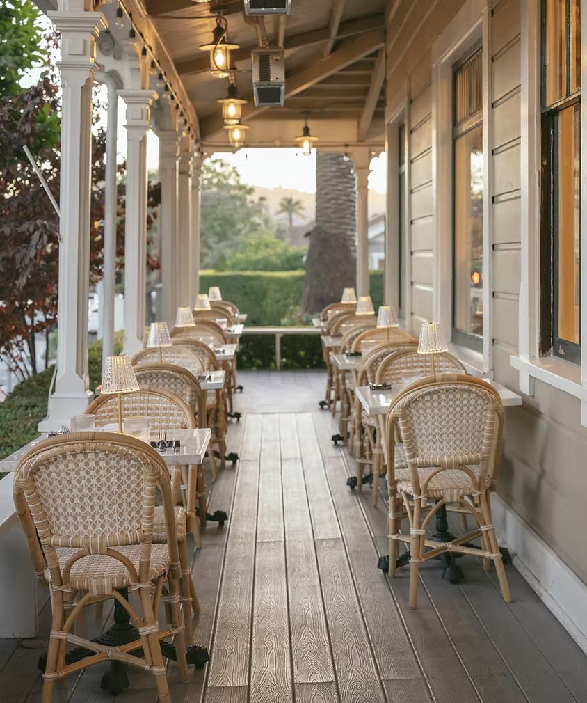 Covered porch with wicker chairs and small round tables lining a wooden walkway