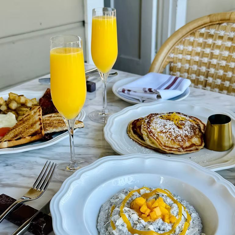 Brunch table with orange juice, pancakes, and toast on white plates outdoors