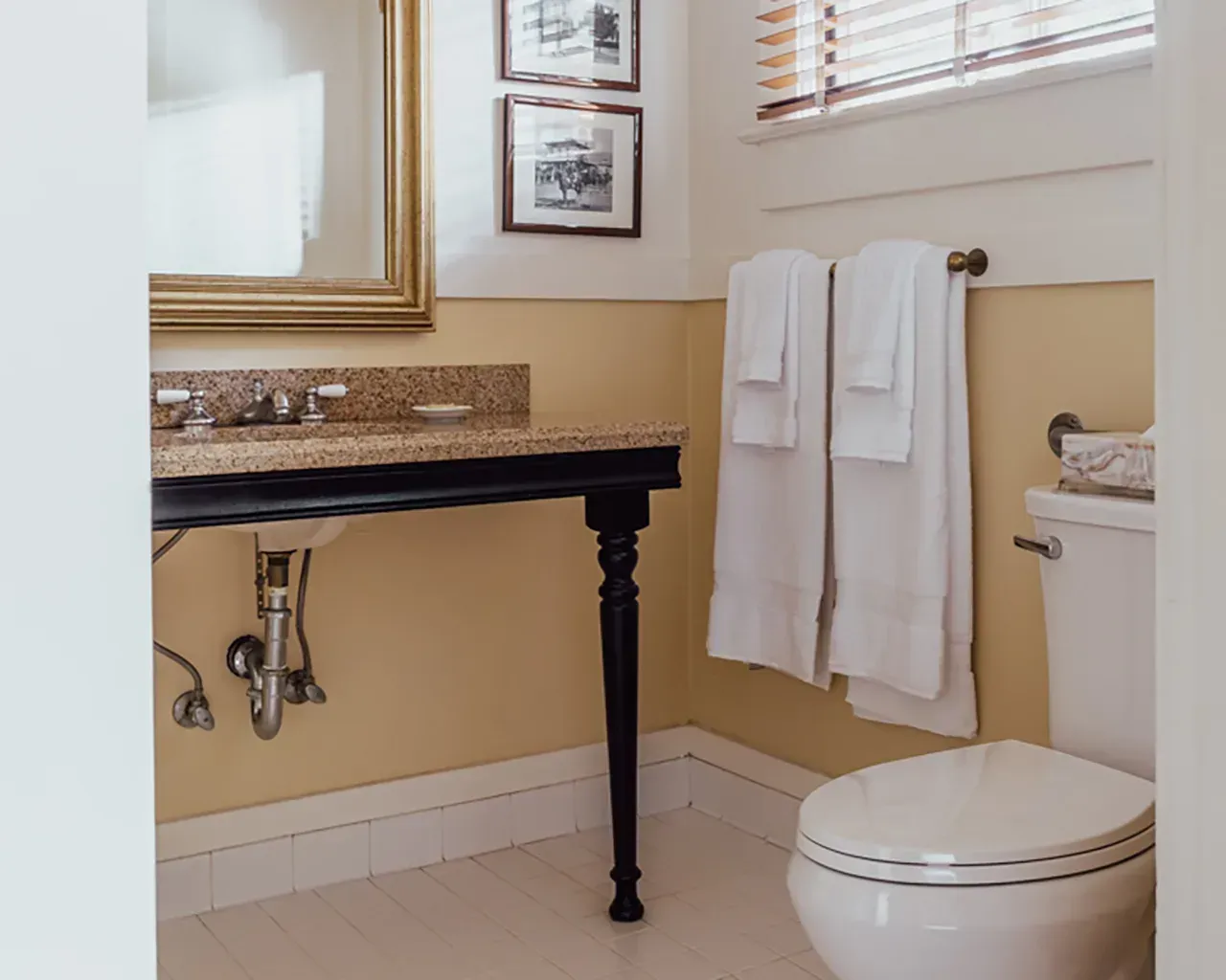 A small bathroom featuring a black pedestal vanity with a granite countertop, beige walls, and a white toilet.