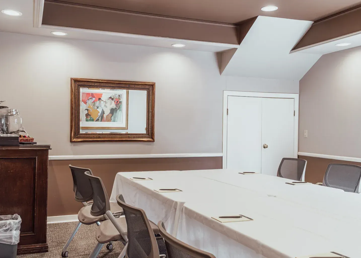 A formal conference room with a large rectangular table covered by a white cloth, surrounded by dark chairs.