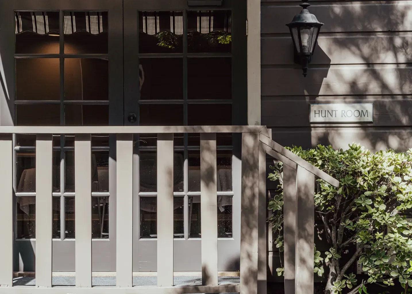 A light gray, railed wooden porch leads to a glass-paneled double door with a lantern and a 