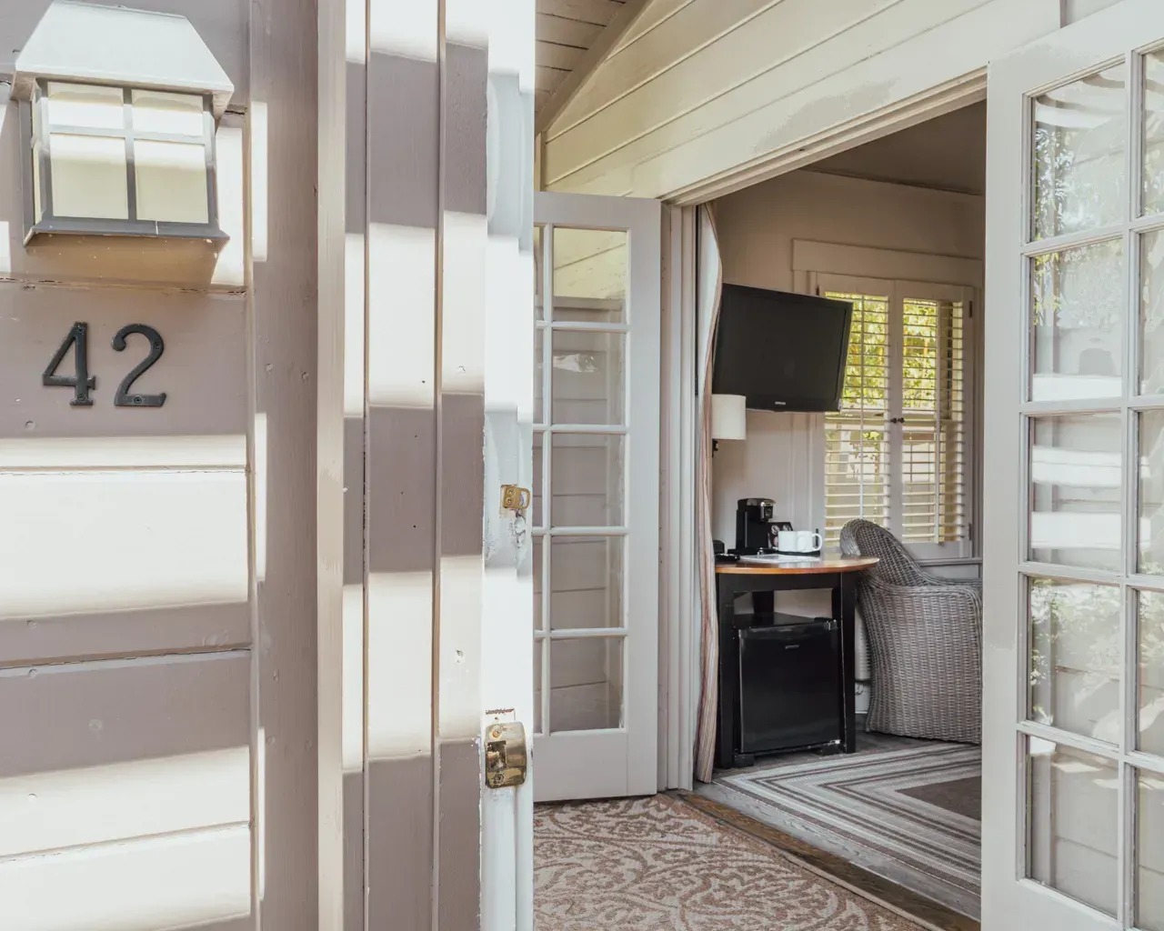View of an open door to a room numbered 42, showing a desk with a TV, a chair, and a patterned rug inside.