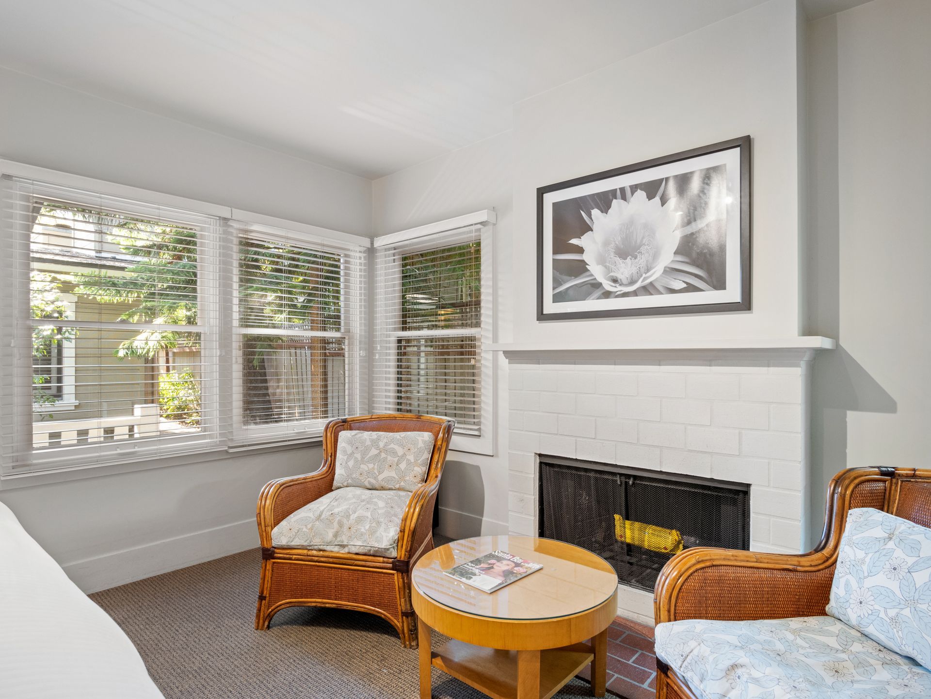 A cozy living room with two wicker armchairs, a round wooden table, and a fireplace with a black-and-white floral print.