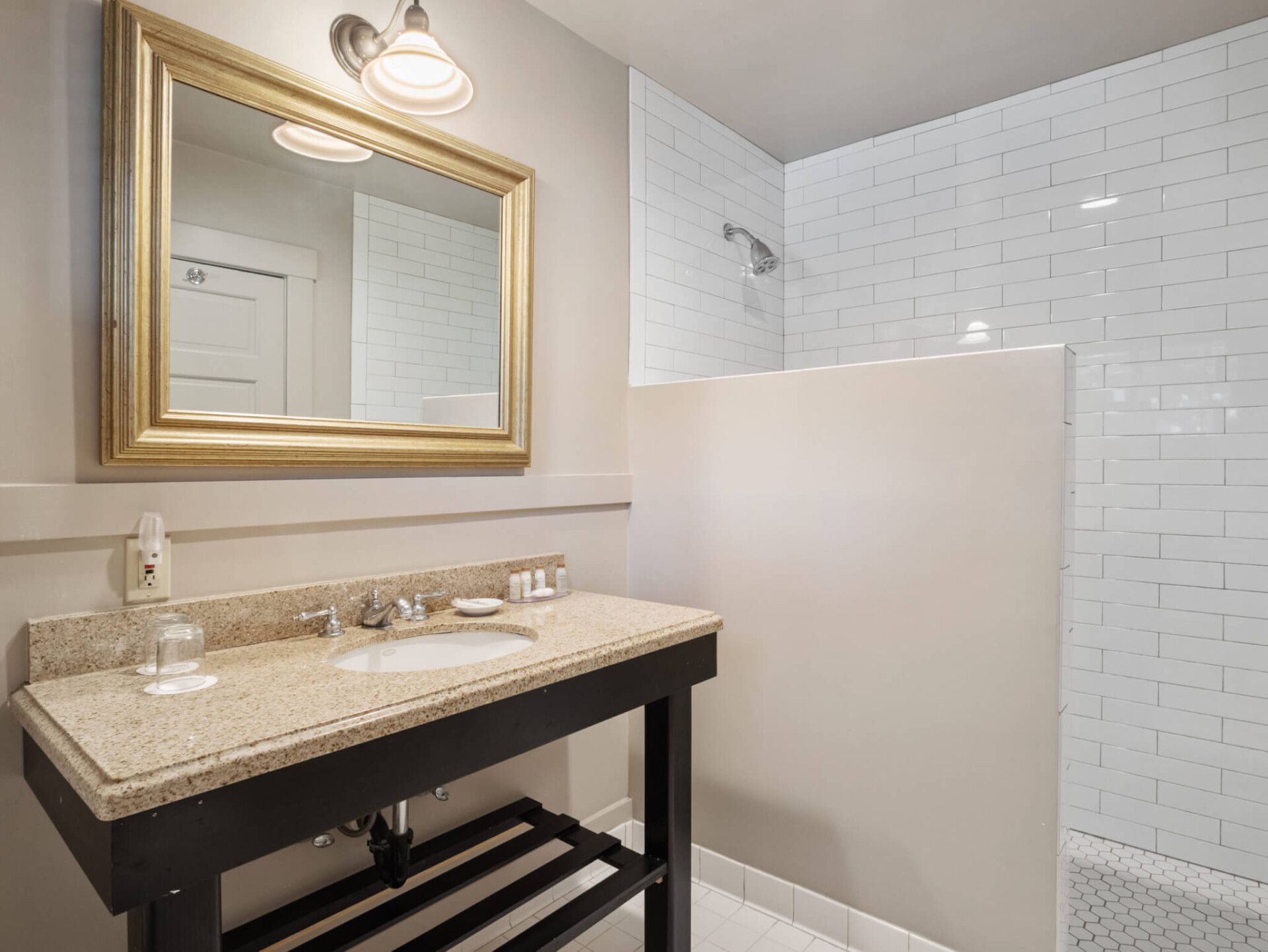 A bathroom vanity with a granite top and gold-framed mirror beside a tiled shower stall.