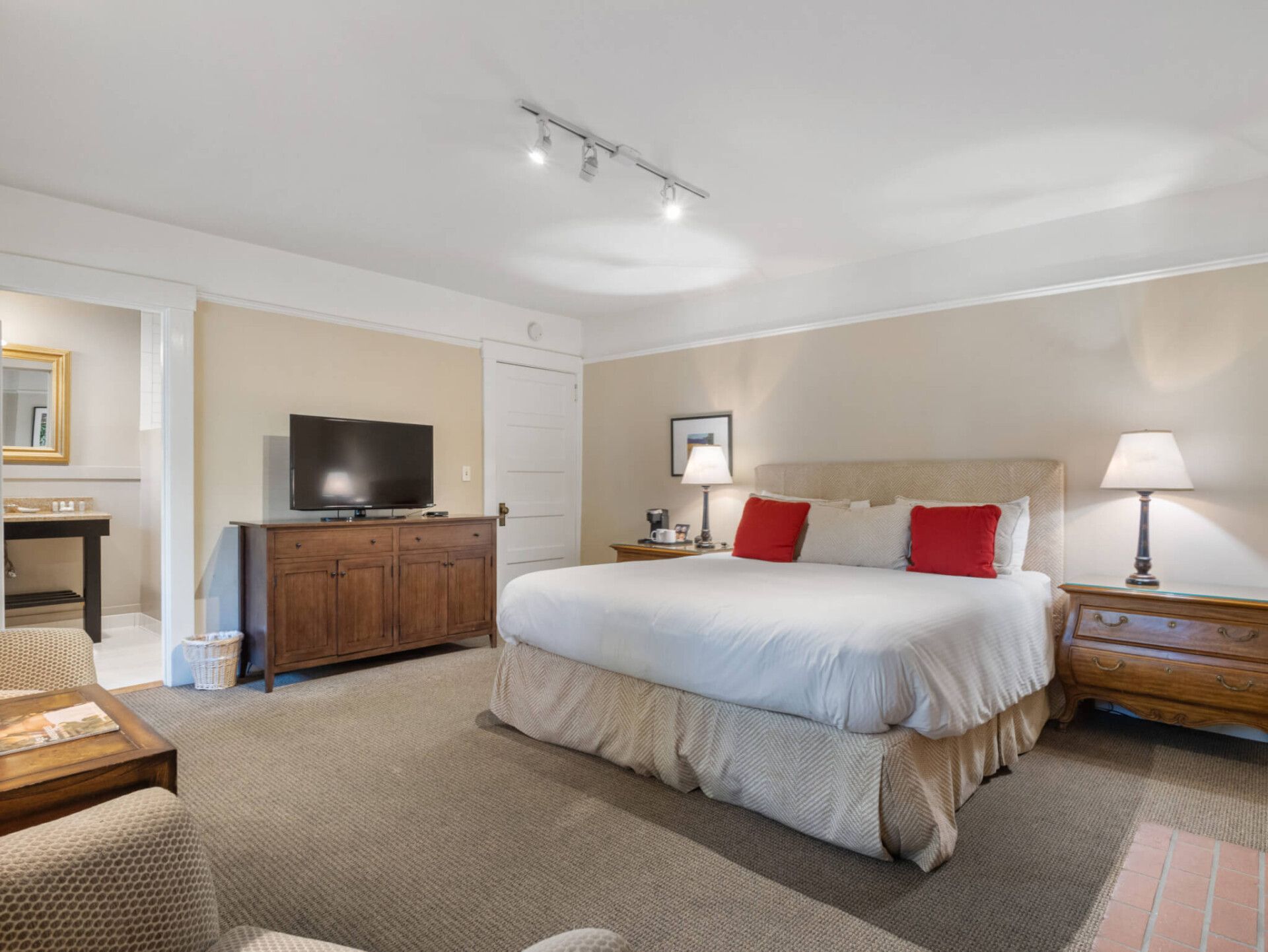 A master bedroom with a large bed, brown wood dresser holding a television, and two matching nightstands with lamps.