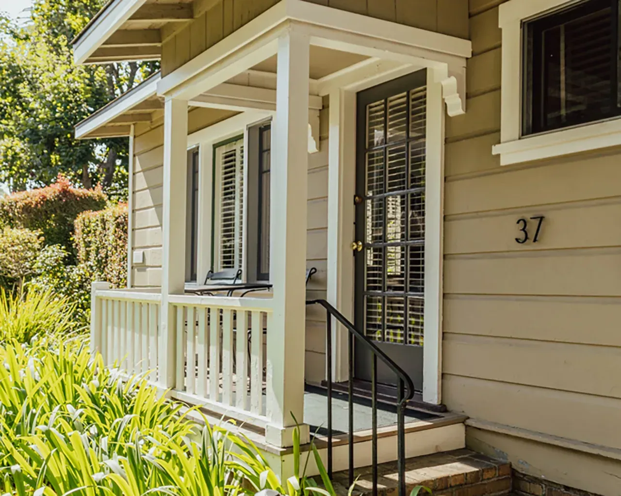 A beige house with a front porch, white railings, a multi-pane glass door, and the number 37 on the exterior wall.