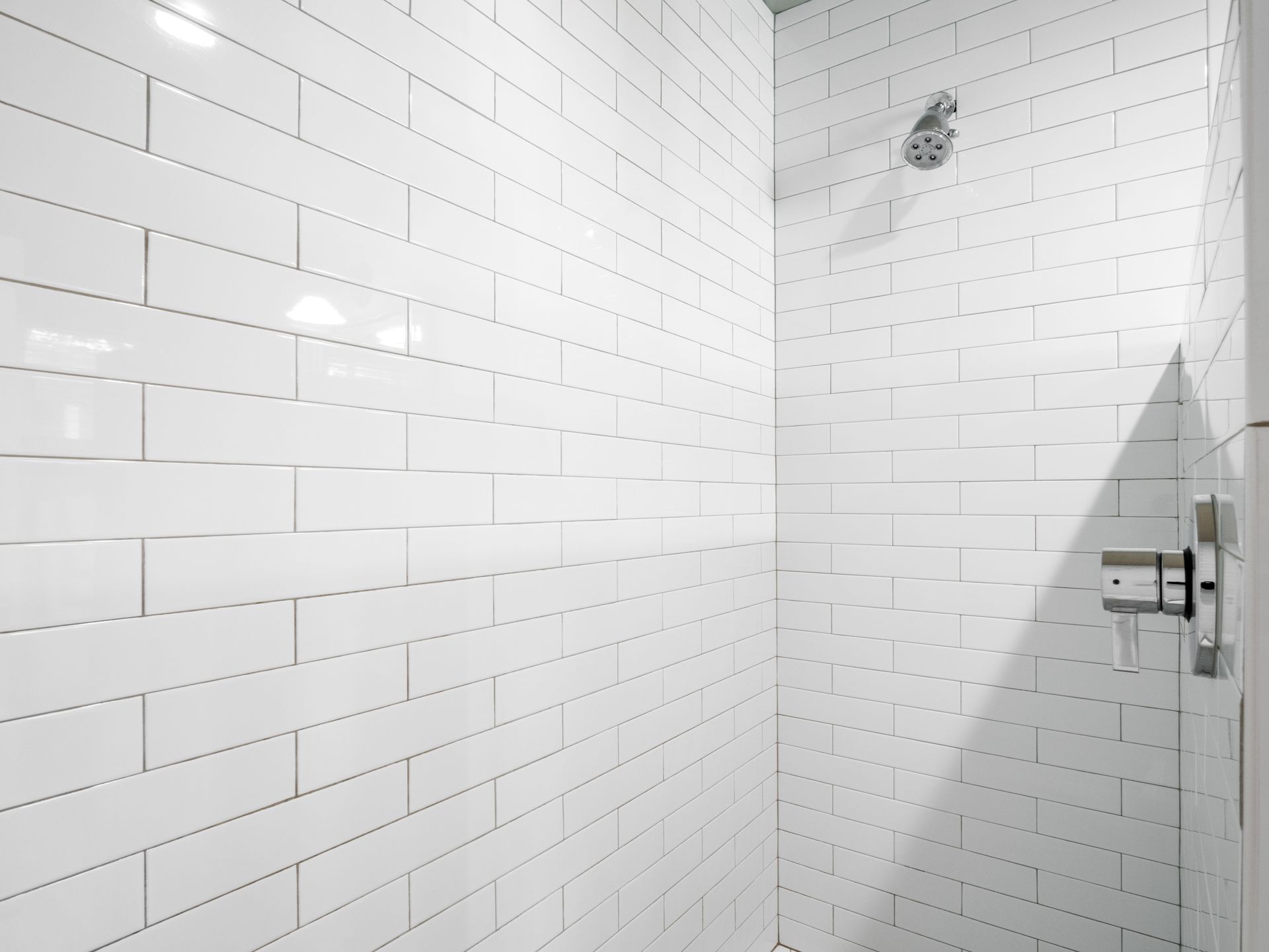 A walk-in shower with white rectangular subway-style wall tiles, a chrome showerhead, and a mounted handle control.