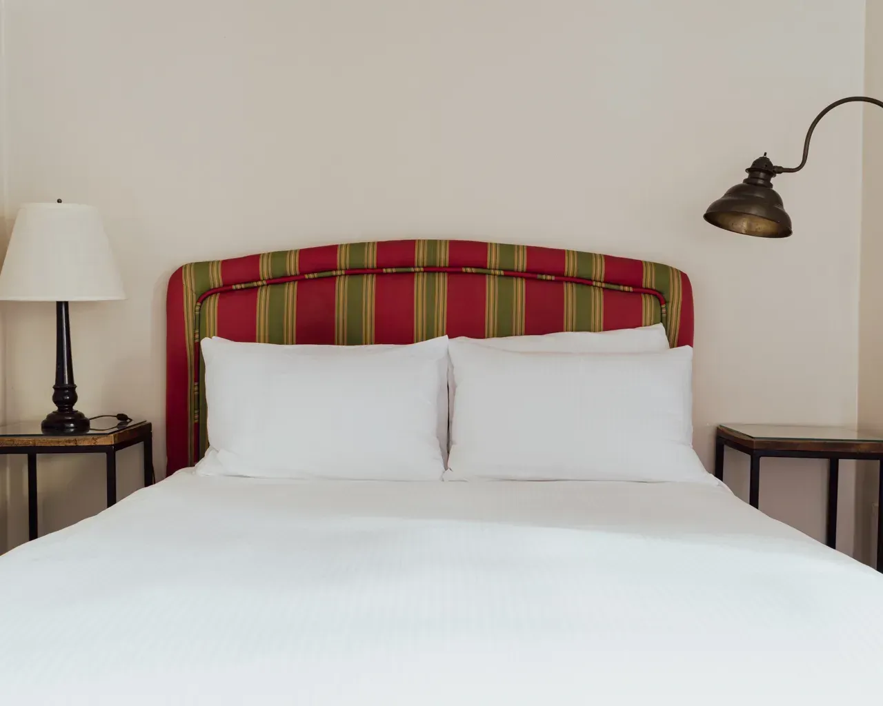 A neatly made bed with white bedding and a striped red and green upholstered headboard between two nightstands.