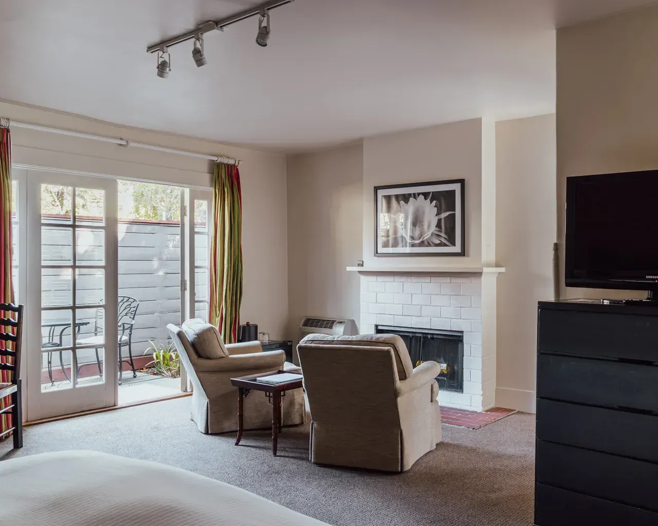 A cozy room featuring two tan armchairs facing a white brick fireplace, with sliding glass doors opening to a patio.