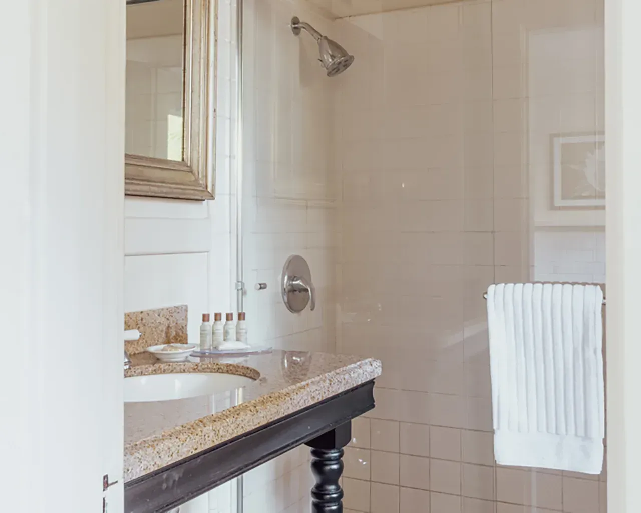 A bathroom with a speckled stone vanity top, black legs, a sink, a wall-mounted mirror, and a glass-enclosed shower.