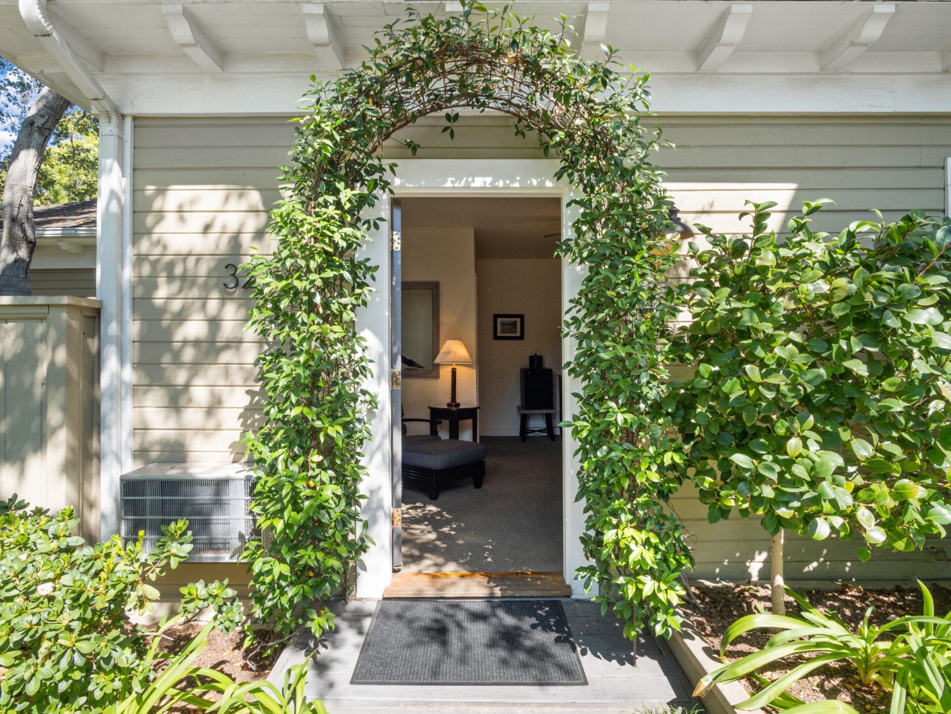 A house entrance featuring an arched doorway covered in green vines, with an open door revealing an interior room.