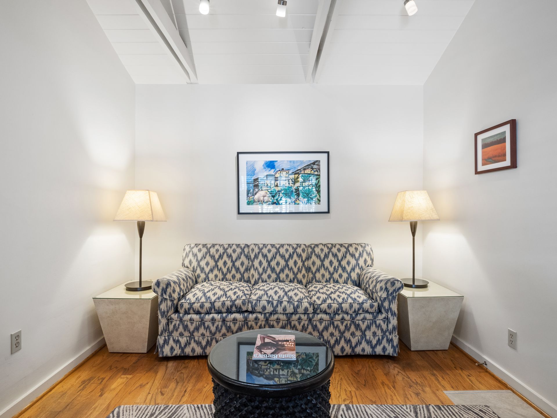 A patterned sofa sits between two lamps and side tables, with a coffee table in front and artwork on white walls.