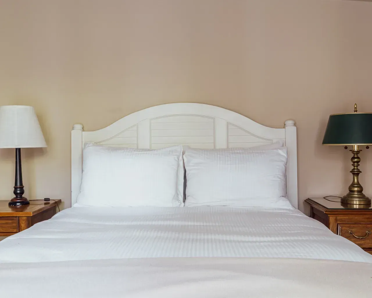 A neatly made bed with white bedding and a white headboard, flanked by two wooden nightstands with lamps.