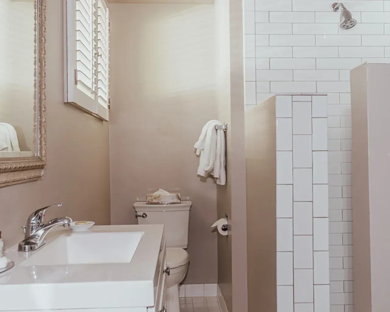 A neutral-toned bathroom featuring a vanity sink, toilet, white tiled shower stall, and a framed mirror.