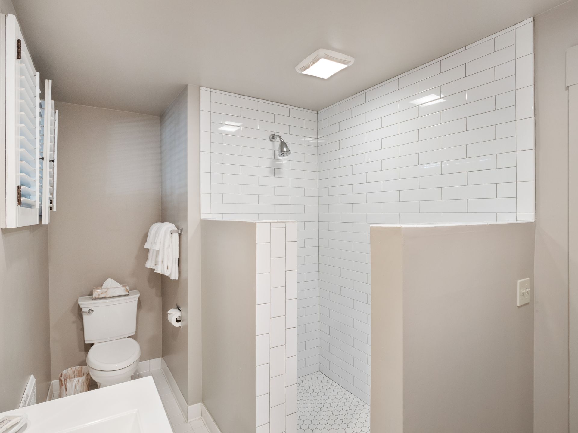 A white tiled walk-in shower stands next to a toilet in a modern bathroom with light gray walls.