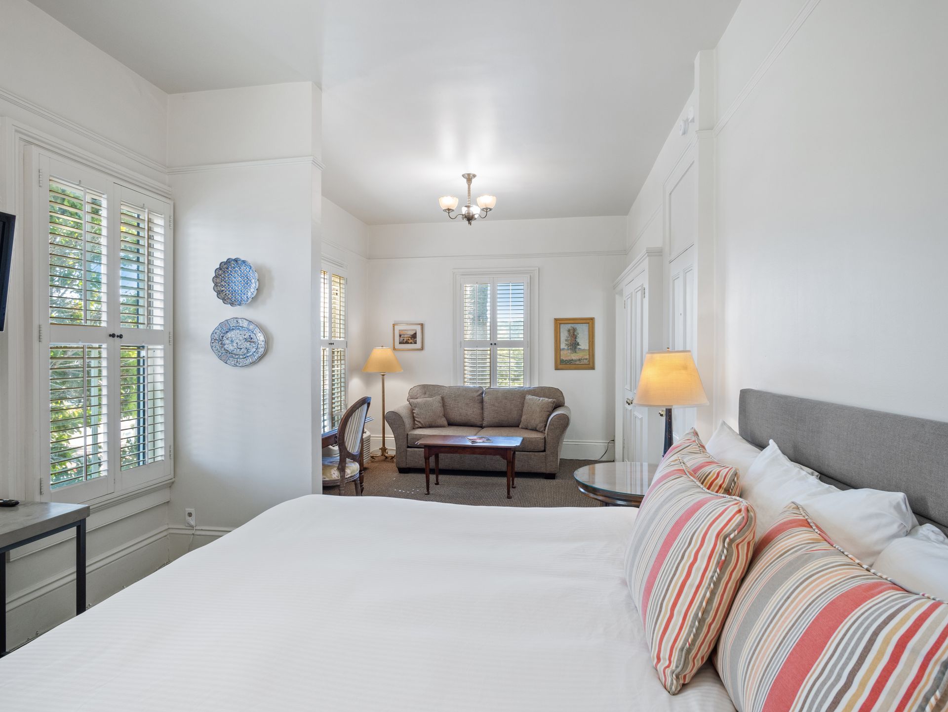A hotel suite with a king-sized bed in the foreground and a separate sitting area with a sofa in the background.