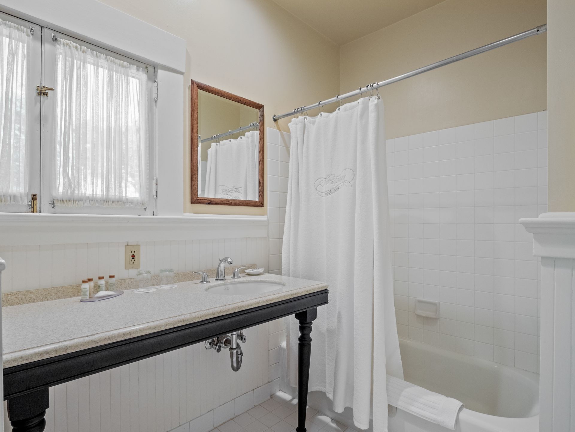 A bathroom with a white vanity, a dark base, a framed mirror, and a shower with a white curtain and white tiled walls.