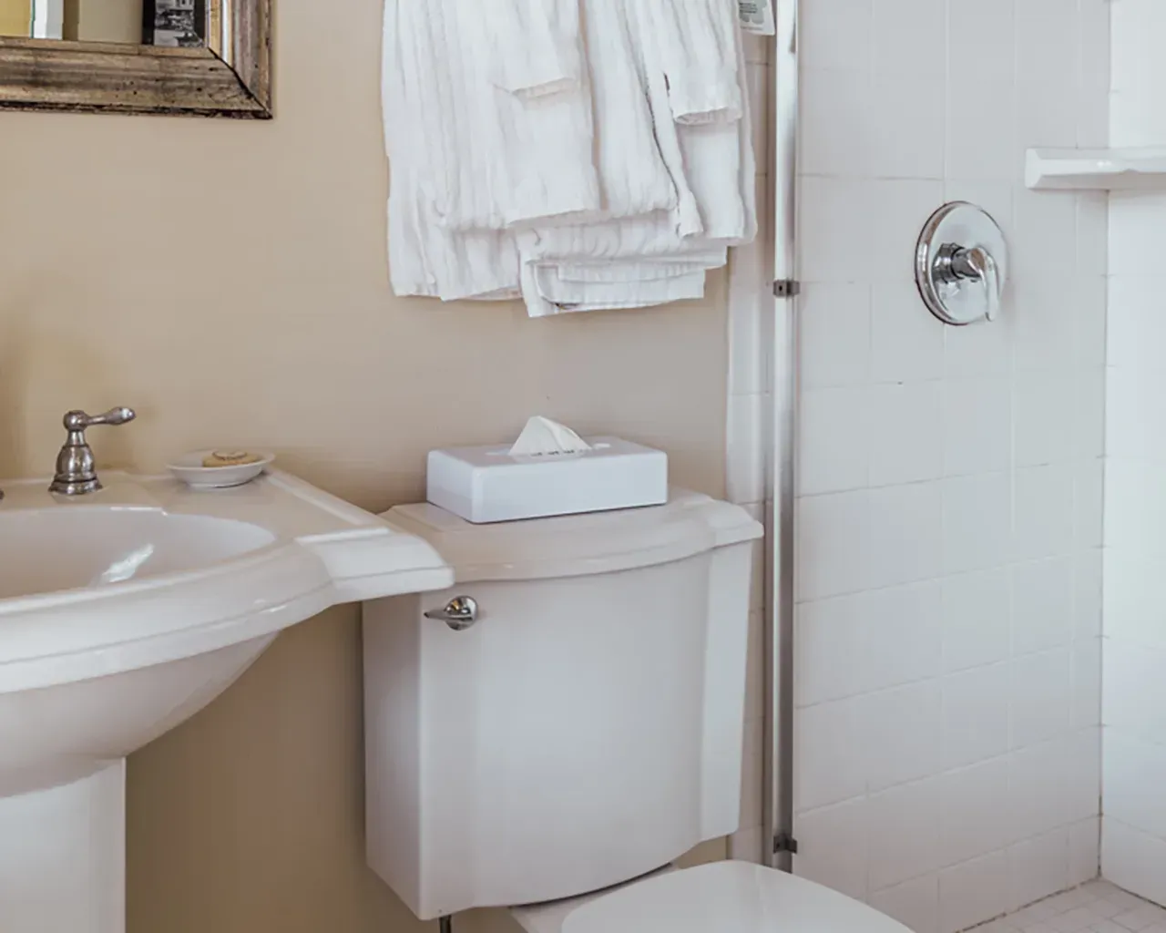 A modern bathroom featuring a white pedestal sink, a toilet with a tissue box on top, and white towels hanging nearby.