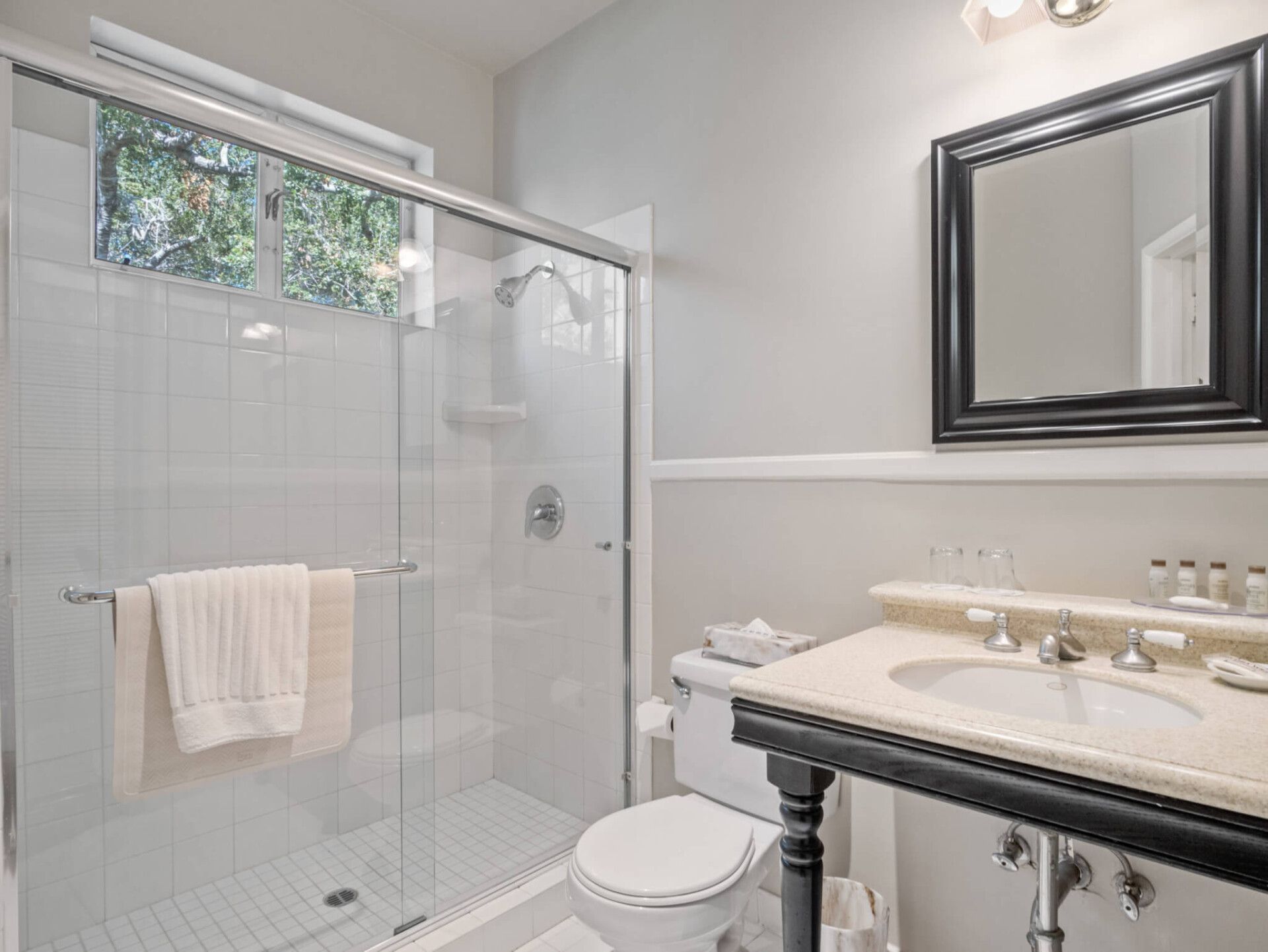 A modern bathroom with a glass-enclosed shower, a white toilet, and a vanity with a black frame and stone countertop.