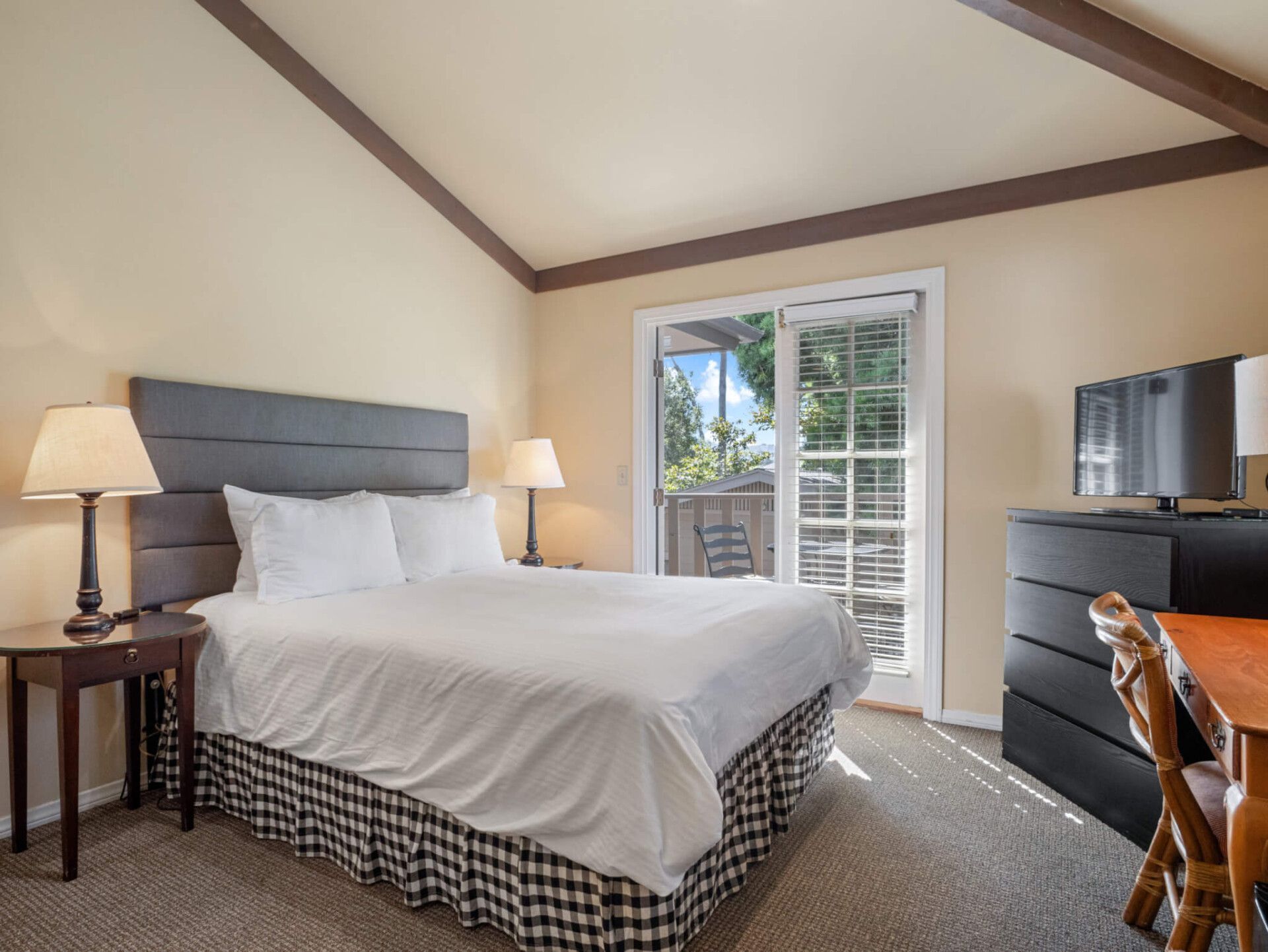 A bedroom featuring a queen bed with white bedding, a gray headboard, two nightstands, a dresser, and glass patio doors.