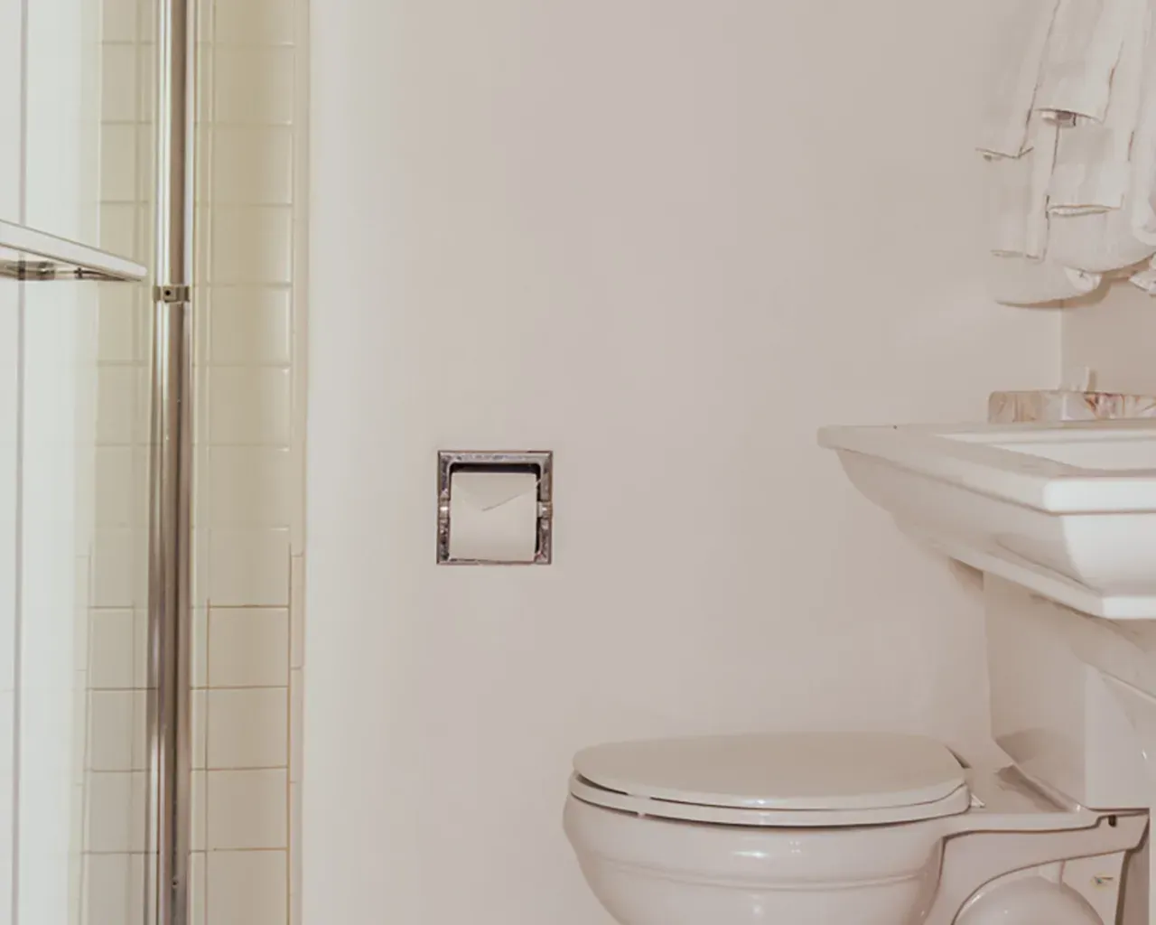 A bathroom interior with a white toilet, a wall-mounted toilet paper holder, and a white sink next to a shower stall.