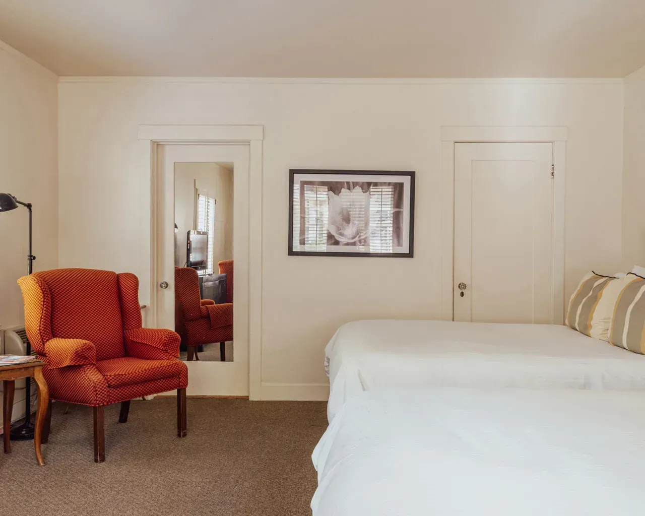 A bedroom with a textured orange armchair, a framed wall picture, a mirror door, and a bed with white bedding.