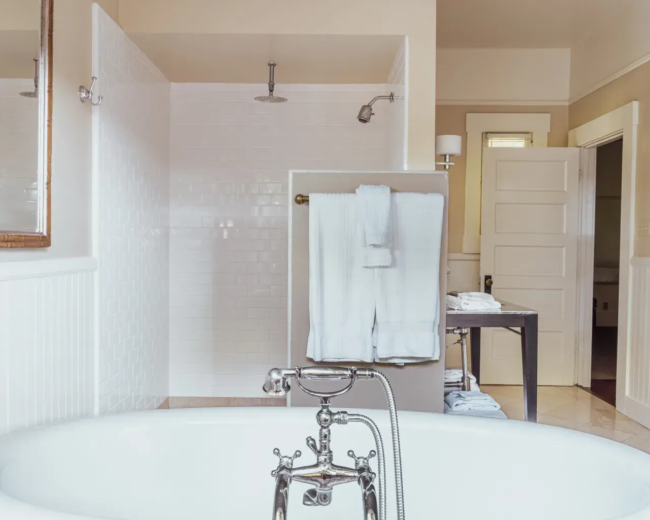 A white claw-foot bathtub with chrome fixtures in a bathroom with a tiled walk-in shower and hanging towels.