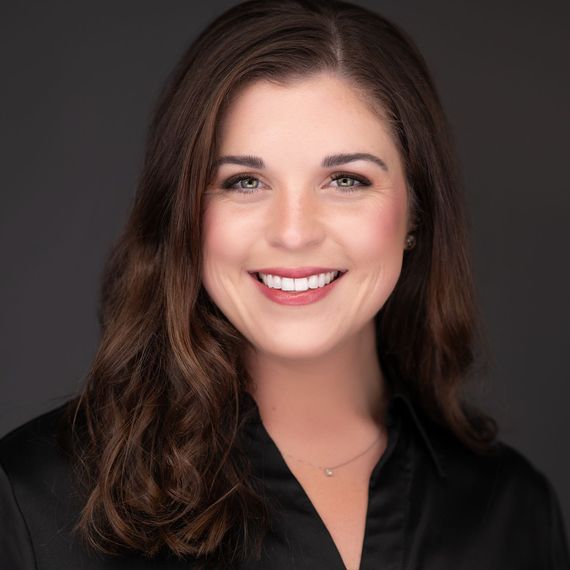 Smiling woman with shoulder-length brown hair against a dark gray studio background